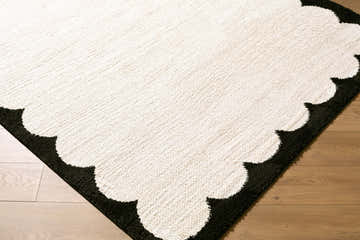 Close up of the Dawa Cream Border rug showing the cream center and black scalloped border on a wood floor. Corner