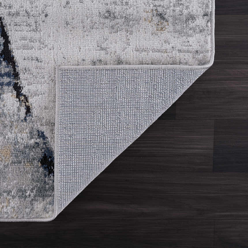 Close-up of the Fremantle Gray Marble Rug showing its cream, gray, gold, and blue abstract pattern and woven backing. Fold