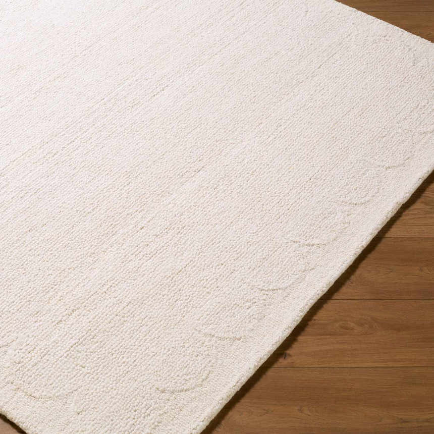 Close-up of the hand-tufted Kazuto Area Rug. Cream wool rug with subtle, carved floral pattern detail. Corner