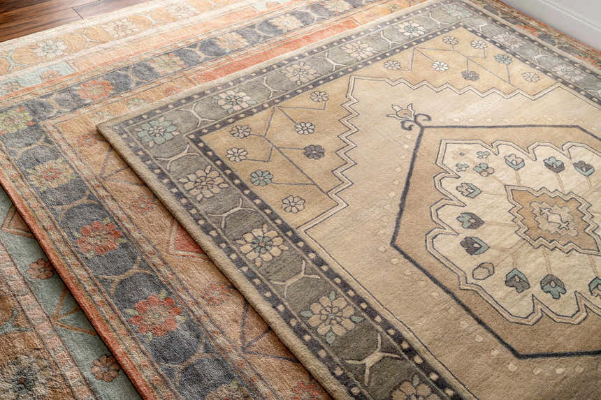 Close-up of two hand-tufted Duckenfield Area Rugs. One is beige, the other is orange with floral patterns. Styleshot