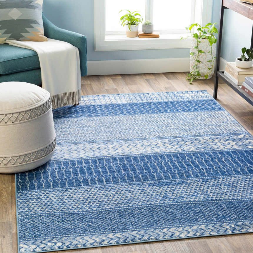 Living room scene with denim and ivory Nampa Area Rug, blue armchair, and neutral ottoman on wood floor. Roomscene-Rectangle