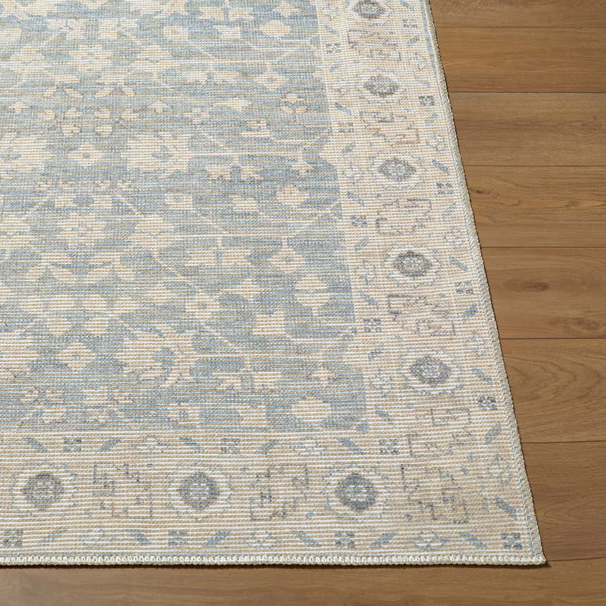 Close-up of Asha Machine Woven Nabela Noor rug showing traditional sky blue and off-white pattern and jute texture on wood floor. Front
