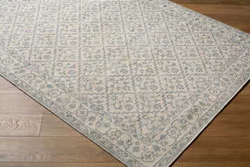 Close-up of the Athiyo Nabela Noor Home x LIVABLISS rug. Off-white rug with a sky blue traditional pattern on wood floors. Corner