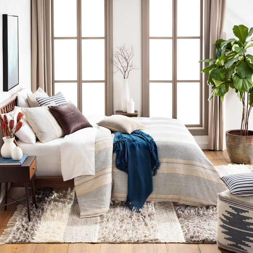 Bedroom scene with a beige and gray Elizabeth Area Rug, wood bed frame, and natural light. Styleshot