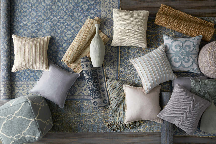 Textured Sherwood Area Rug in ice blue with pillows, pouf, and rolled rugs on a wood floor. Styleshot