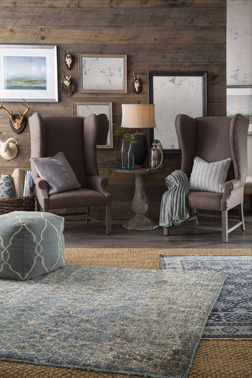 Rustic living room scene with a blue Sherwood Area Rug, brown wingback chairs, and wood paneled walls. Roomscene-Rectangle