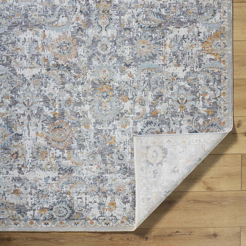 Close-up of the Atara Area Rug. Traditional floral pattern in cloud gray, dark brown, and nutmeg on a wood floor. Fold