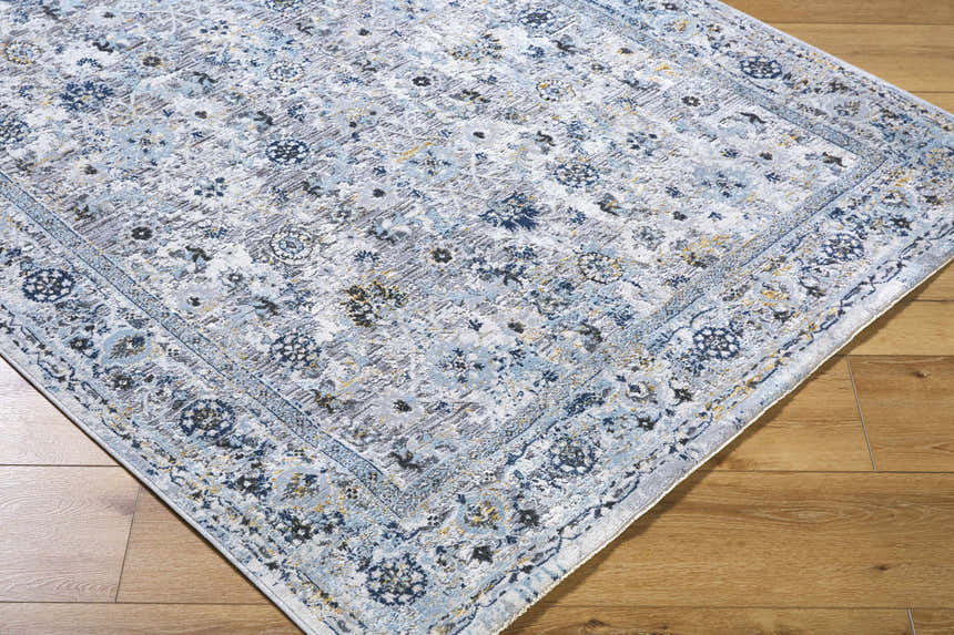 Close-up of the Irida Area Rug showcasing its denim, gray, and nutmeg traditional floral pattern and machine-woven texture. Corner