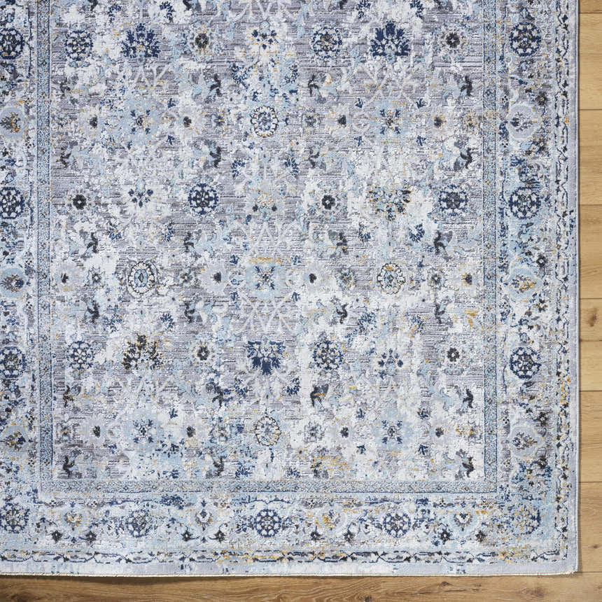 Close-up of the Irida Area Rug showing its denim, gray, and nutmeg floral pattern and machine-woven texture. Corner