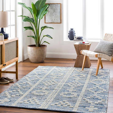 Living room scene with a blue and white Suna Area Carpet, wood furniture, and a large potted plant. Roomscene-Rectangle