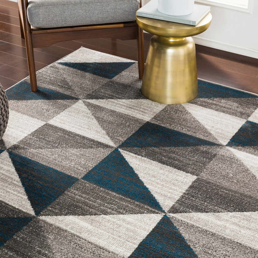 Living room scene with gray chair, gold side table, and blue, gray Volant Area Rug with geometric design. Roomscene-Rectangle