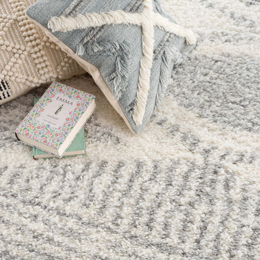 Close-up of the plush Trunding Area Rug in Gray, featuring a geometric pattern and soft, shaggy texture. Neutral pillows and books accent. Styleshot