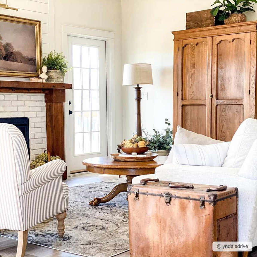 Living room scene with a Georgiana Area Rug in beige, black, and gray under a round wood table. Farmhouse style. Roomscene-Rectangle