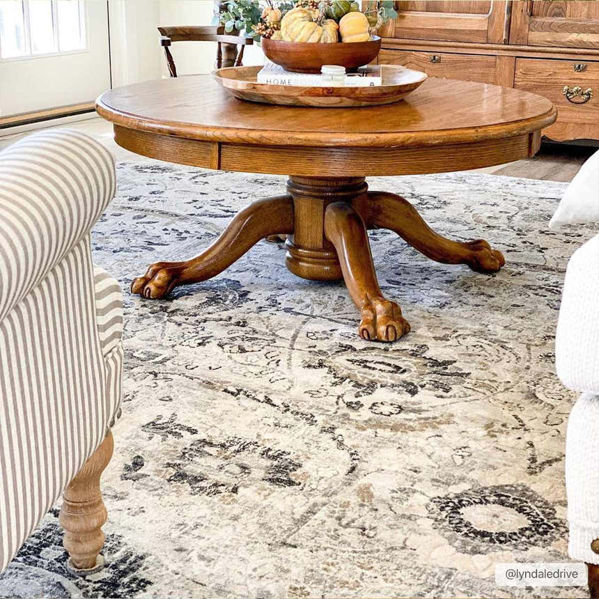 Living room scene with a round wood table on a Georgiana Area Rug. The rug has beige, black, and gray tones. Styleshot