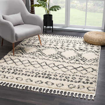 Living room scene with a bone and brown Duncans Area Rug, gray chair, and woven pouf. Moroccan style rug with tassels. Roomscene-Rectangle