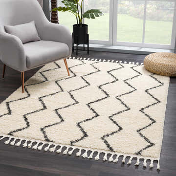 Living room scene with a West End Plush Area Rug in light beige and charcoal, gray chair, and woven ottoman. Roomscene-Rectangle