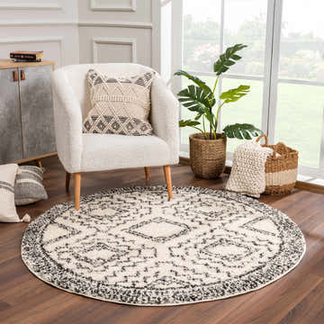 Cozy living room scene with round Buan Area Rug in charcoal and cream, textured chair, and natural light. Roomscene-Round