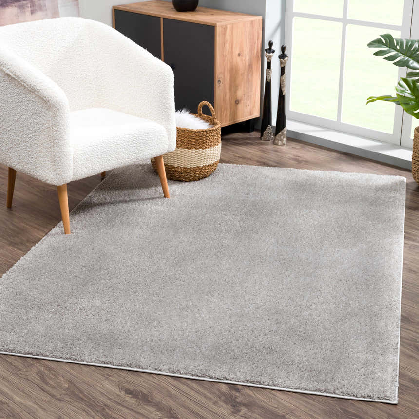 Living room scene with a Judy Solid Gray Washable Shag Rug, white armchair, wood cabinet, and a bright window. Roomscene-Rectangle