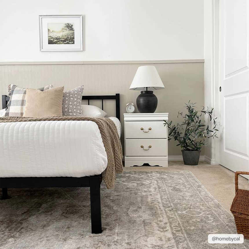 Bedroom scene with a light gray Gael Boutique Washable Rug, black bed frame, white nightstand, and neutral decor. Roomscene-Rectangle