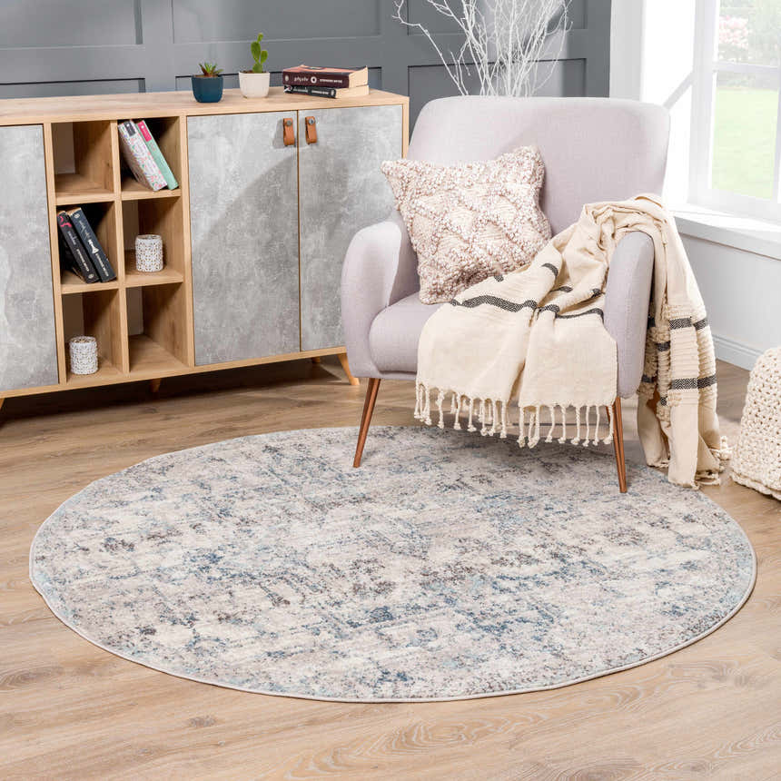 Living room scene with a round Orrick Area Rug in blue, cream and gray, styled with a chair, cabinet, and wood floors. Roomscene-Round