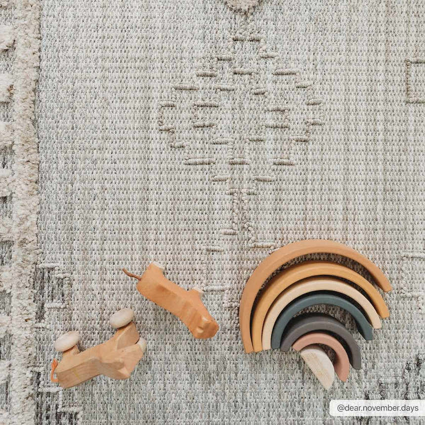 Close-up of the Amaga High-Low Rustic Rug in light beige with geometric pattern and neutral wood toys. Styleshot