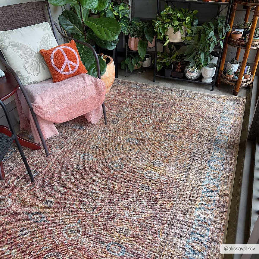 Boho porch scene with Anshu Peach Washable Area Rug, potted plants, and cozy chair with peach throw and peace sign pillow. Roomscene-Rectangle