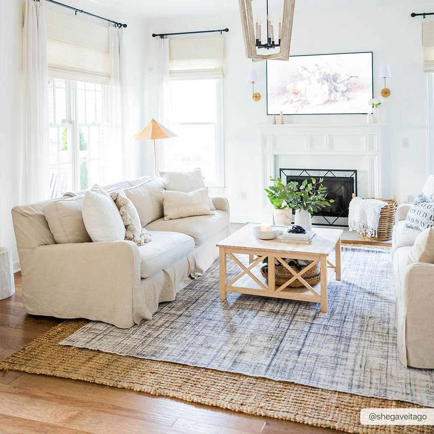 Bright living room with layered rugs: jute rug under the Taysan Area Rug. Beige sofas, wood coffee table, and white fireplace. Roomscene-Rectangle