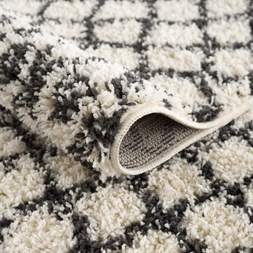 Close-up of the Muni Berber Shag Rug, showcasing its charcoal and light beige colors and plush, textured shag design. Fold
