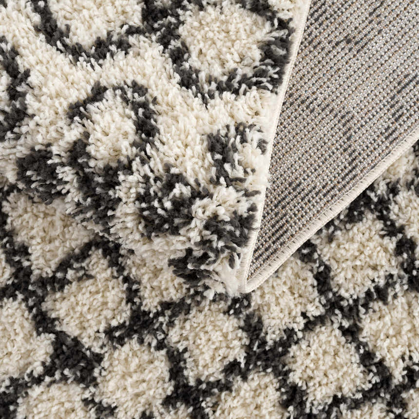Close-up of the Muni Berber Shag Rug showing charcoal and light beige colors and shag texture. Machine woven construction detail. Fold