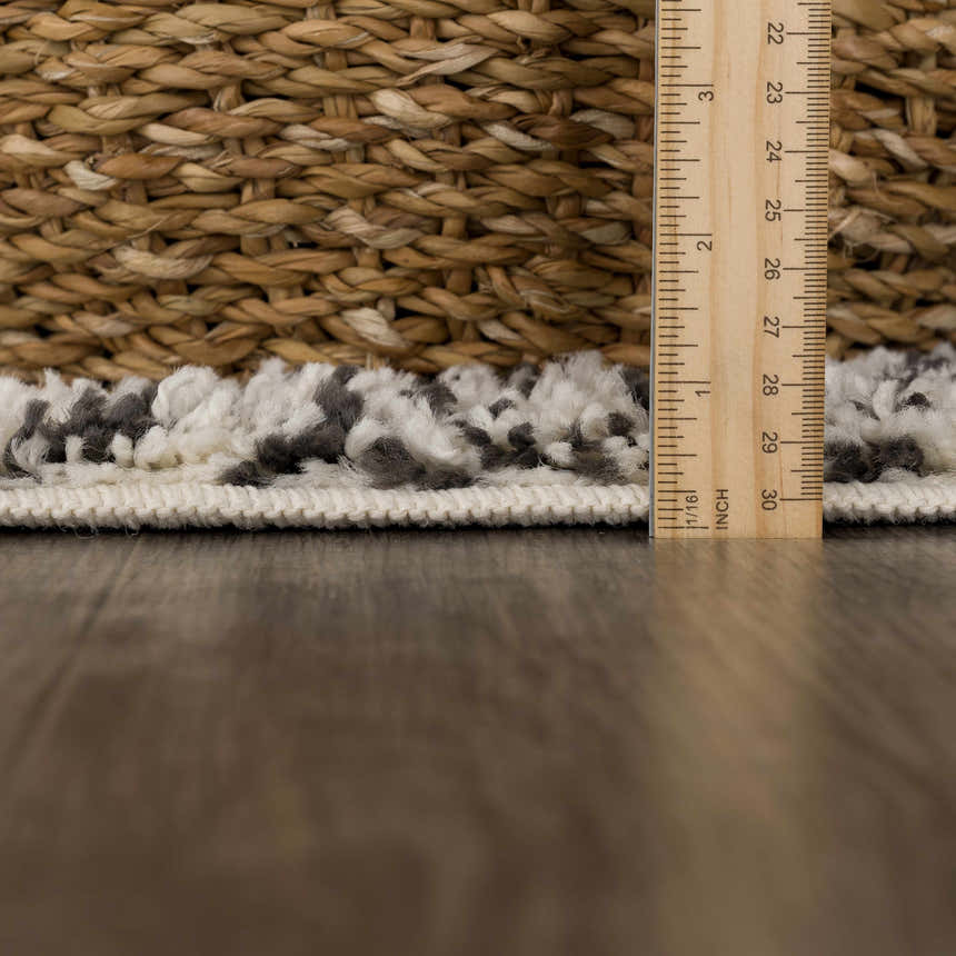 Close-up of the Fishhook Berber Shag Rug showing its dark gray and lambswool colors, shag texture, and thickness with a ruler. Pile