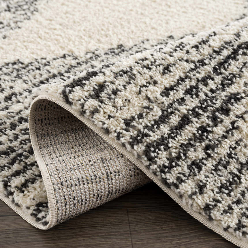 Close-up of the Howth Area Rug showcasing its bone and dark gray shag texture and machine-woven construction. Fold