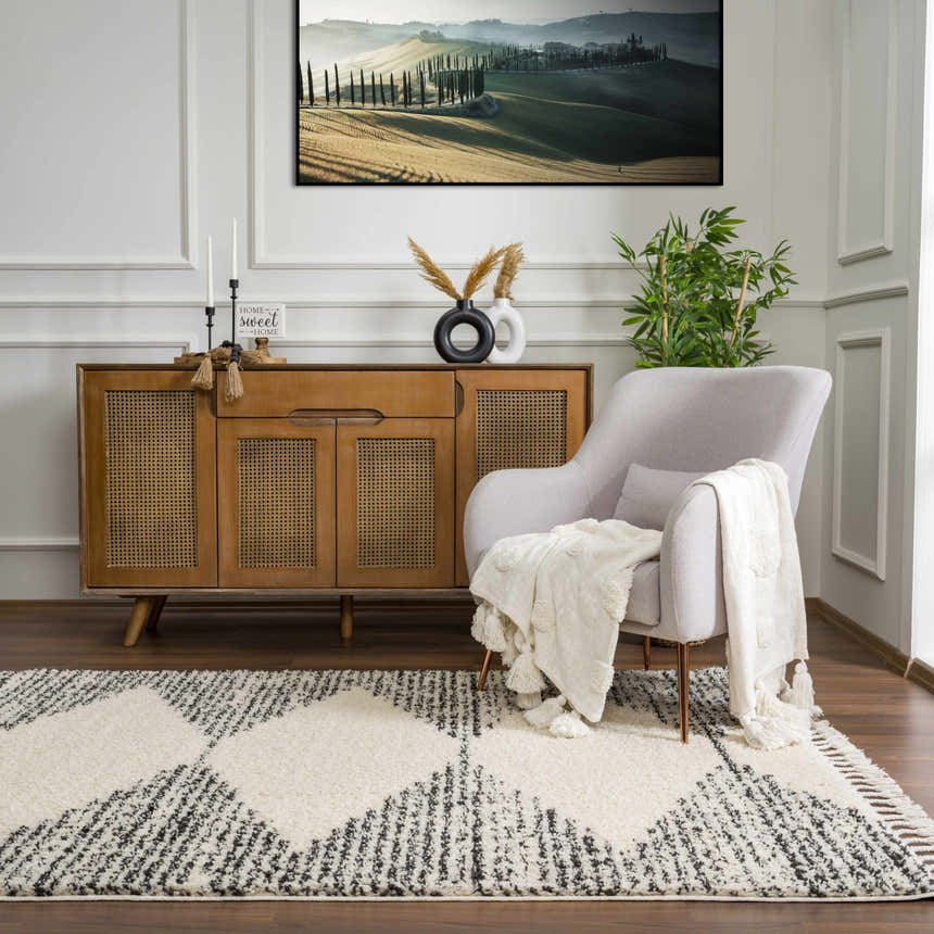 Living room scene with a bone and dark gray Howth Area Rug, light gray chair, and wood cabinet. Roomscene-Rectangle