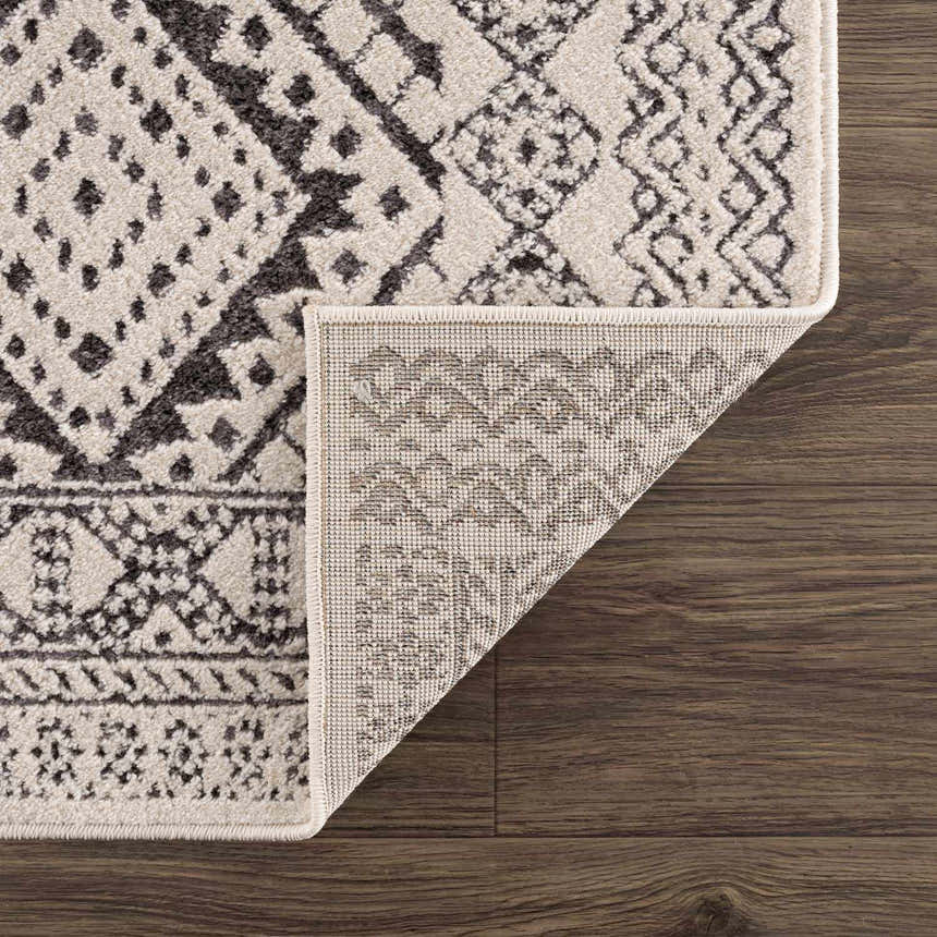 Close-up of the Merriott Area Rug showing the charcoal, beige, and brown bohemian pattern and machine-woven texture. Fold