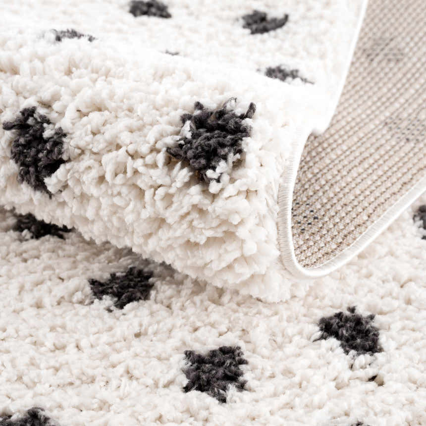 Close-up of the plush Chaia Dotted Black & White Rug, showing its soft texture, black dots, and machine-woven backing. Fold