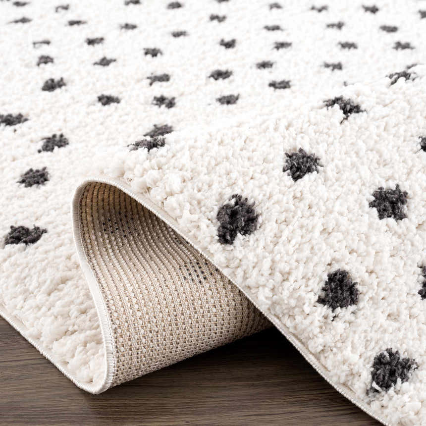 Close up of the Chaia Dotted Black & White Plush Rug showing its soft shag texture and dotted animal pattern. Fold