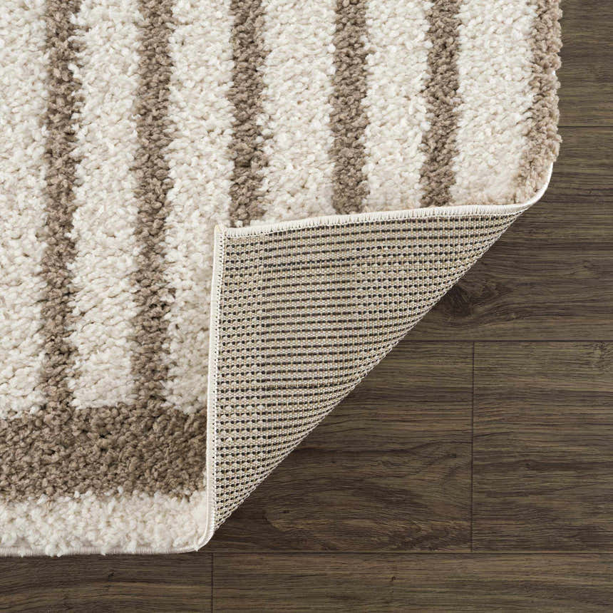 Close up of the Jola Beige Area Rug showing its beige and white stripes, shag texture, and backing on dark wood floor. Fold