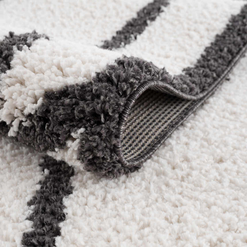 Close-up of the Brad Area Rug, a shag rug with a black and white striped design and visible rug backing. Fold