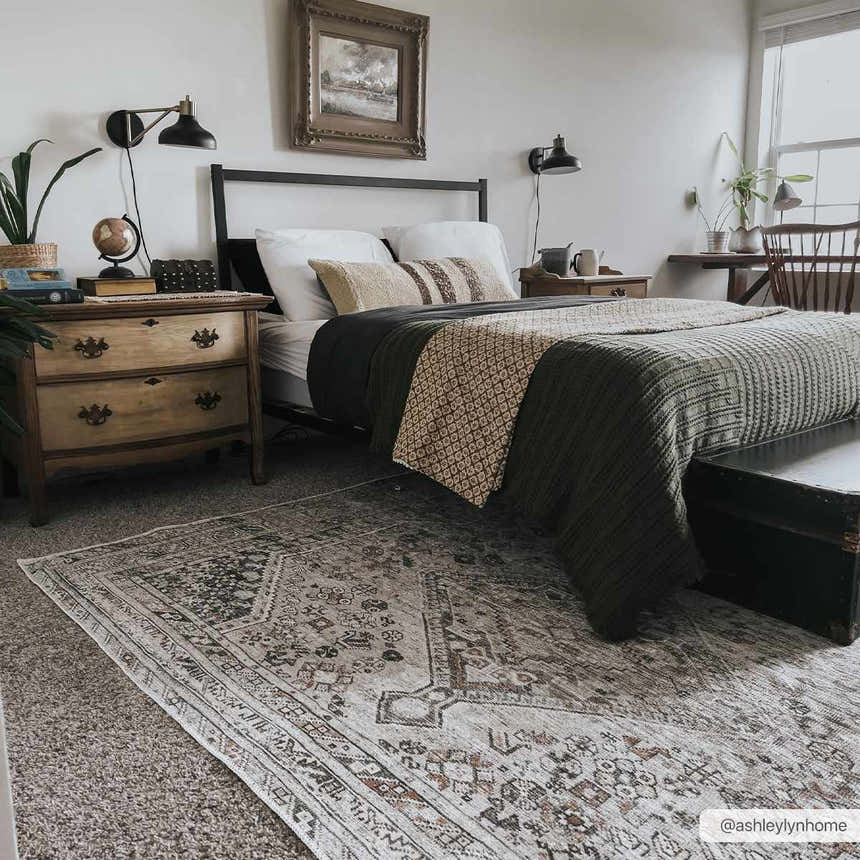 Bedroom scene with a Barny Beige Flat Pile Washable Rug, black bed frame, wooden dresser, and neutral tones. Roomscene-Rectangle