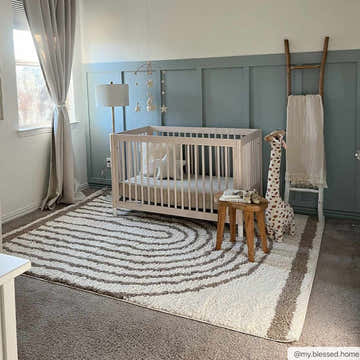 Nursery scene with a beige crib on a Jola Beige Area Rug with a geometric swirl pattern. Blue accent wall. Roomscene-Rectangle