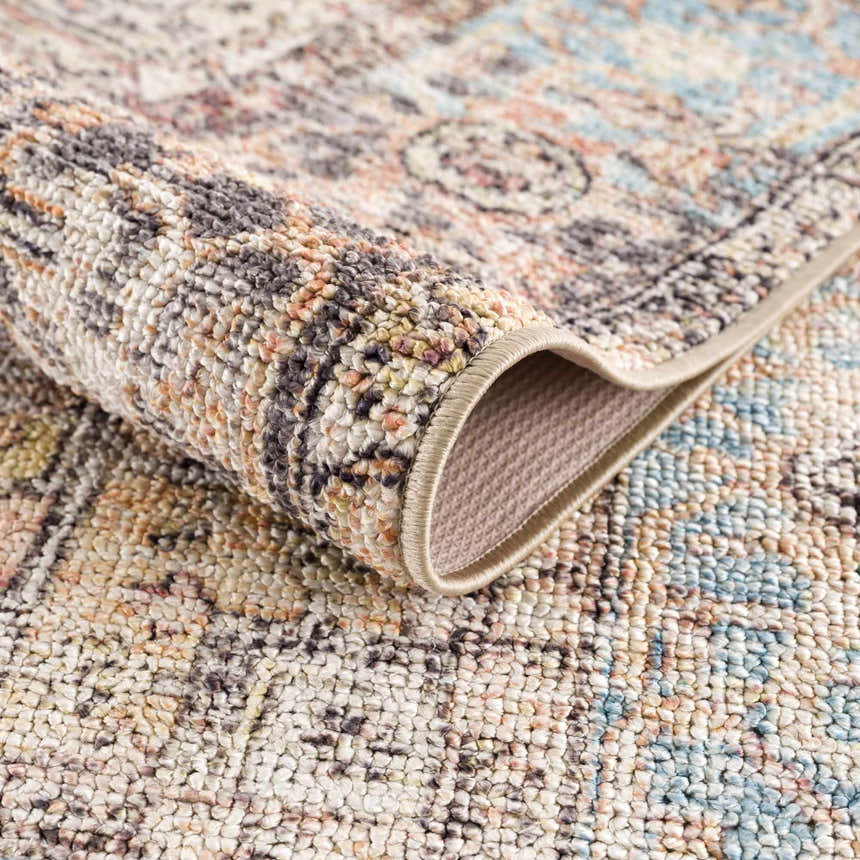 Close-up of the Beck Peach Washable Area Rug showing the traditional pattern, beige, blue, and peach colors, and woven texture. Fold