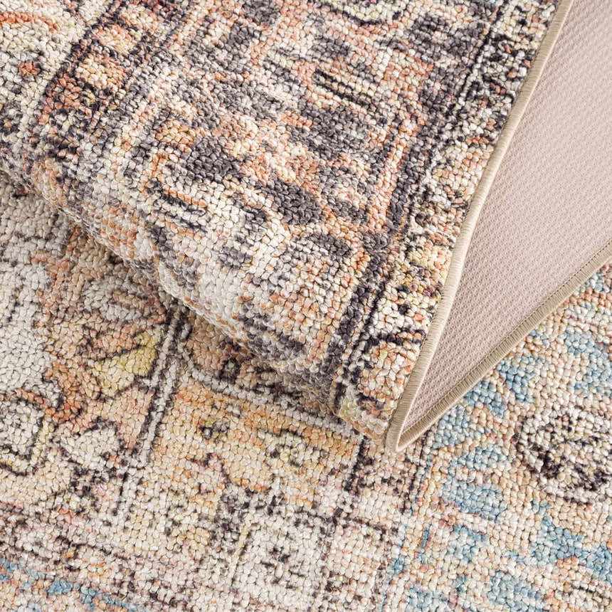 Close-up of the Beck Peach Washable Area Rug showing its traditional pattern, peach, beige, blue, and brown colors. Fold