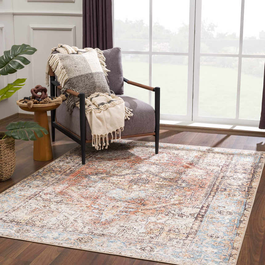 Living room scene with a Beck Peach Washable Area Rug, gray chair, throw blanket, wood floors, and natural light. Roomscene-Rectangle