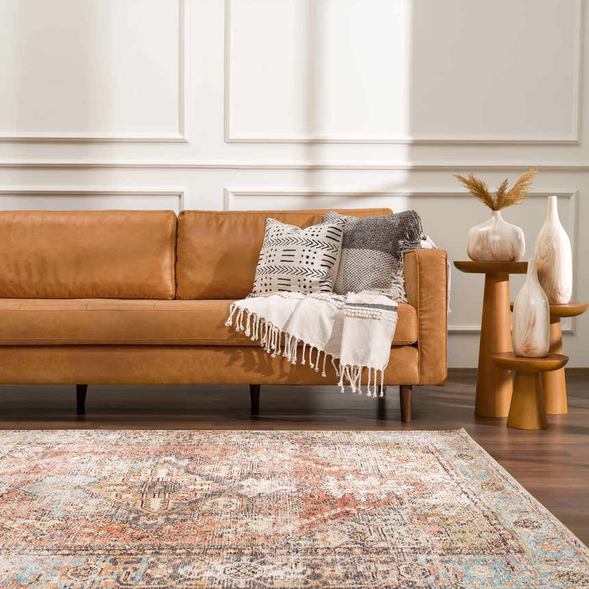 Living room scene with a Beck Peach Washable Area Rug, tan leather sofa, and wood side tables with decorative vases. Roomscene-Rectangle