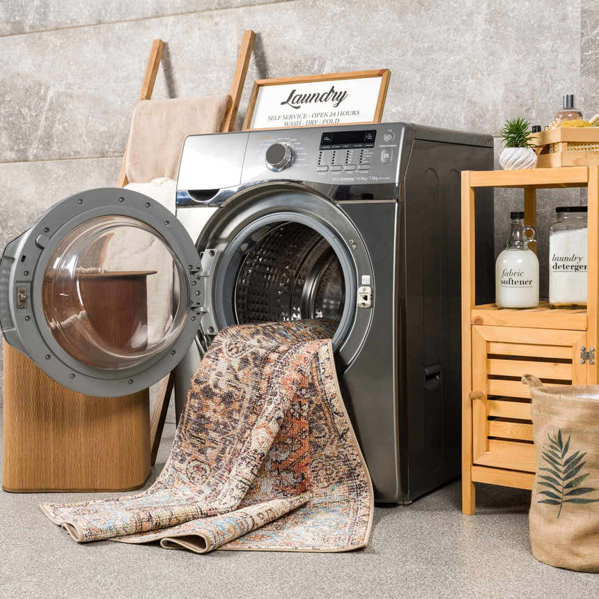 Laundry room scene with Beck Peach Washable Area Rug spilling from the washing machine, next to a wooden shelf and laundry basket. Washing-Machine