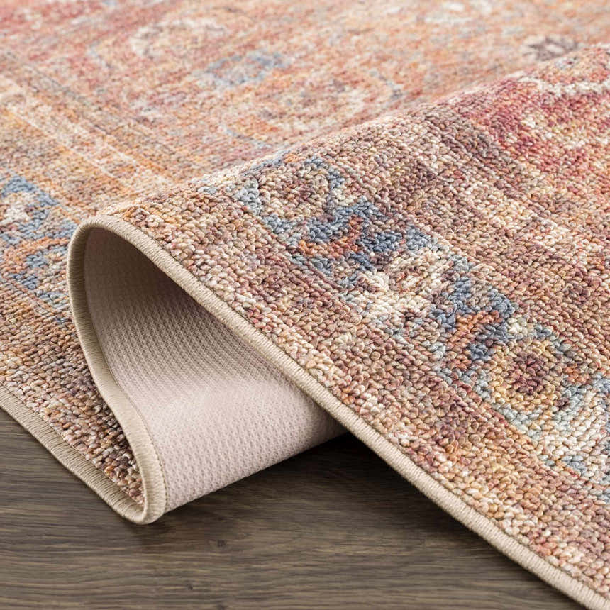 Close-up of the Anshu Peach Washable Area Rug showing its traditional vintage design, beige, blue, and burgundy colors, and soft texture. Fold