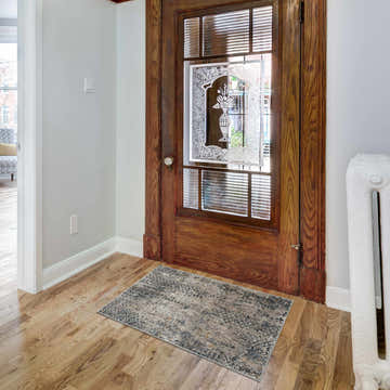 Entryway scene with a beige and blue Lawnton Area Rug. Wood floors and door, white walls. Roomscene-Rectangle