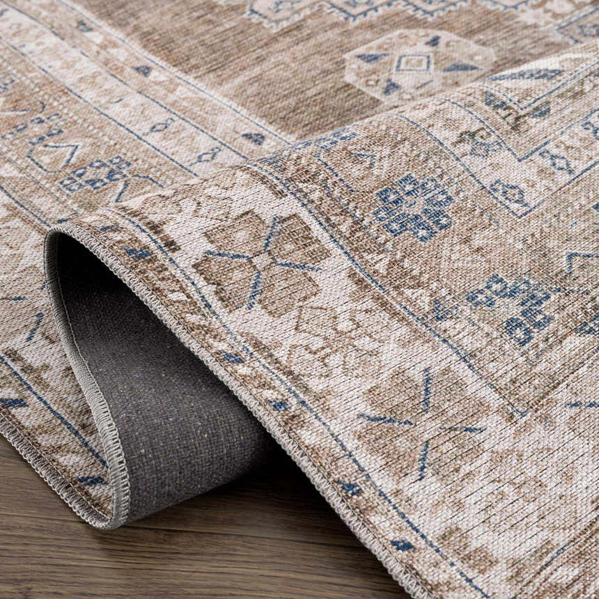 Close up of the Baltinglass Flat Pile Washable Rug. Features a traditional oriental pattern in blue, cream, and beige tones. Fold
