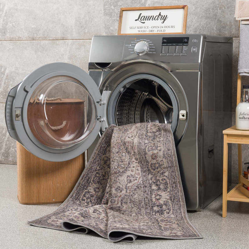 Laundry room scene with a Greenpoint Dusty Blue Washable Rug partially inside a washing machine. Beige, black, and sage colors. Washing-Machine