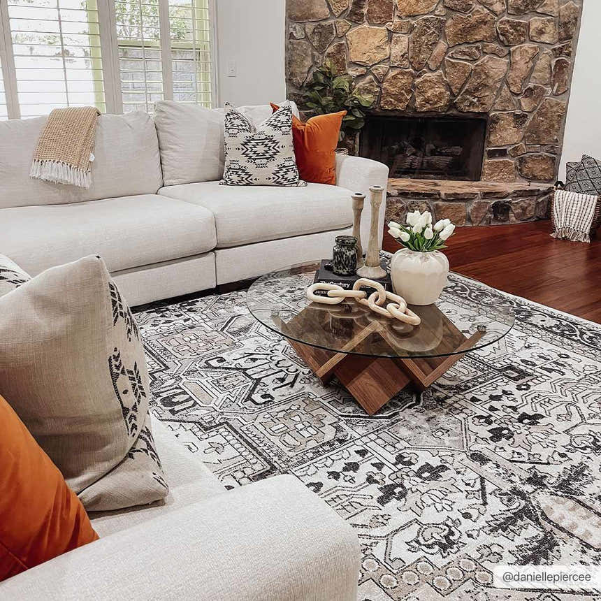 Living room scene with a Cabacungan Washable Area Rug in black, gray, and beige under a glass coffee table. White sofa. Stone fireplace. Roomscene-Rectangle