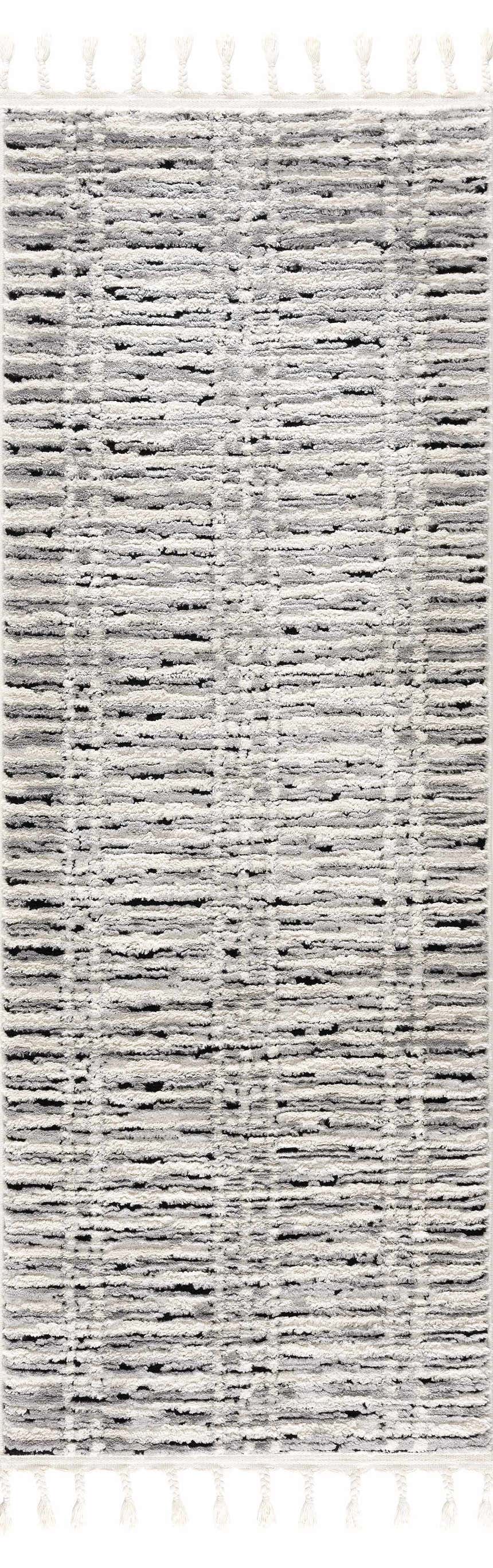 Close-up of the Nava Area Rug. Beige, bone, and black geometric pattern. Tassels on the ends. Design-Runner